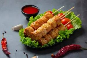 烤肉串放在生菜上，搭配櫻桃番茄，配一小碗紅色蘸醬和乾辣椒。.