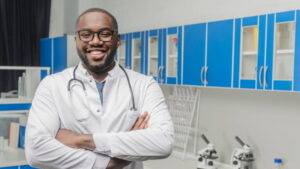 一位穿著白大褂、戴著聽診器的醫生站在實驗室中，背景是藍色的櫥櫃和兩台顯微鏡。.