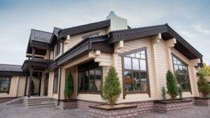 一棟現代化的兩層樓房，有大窗戶、米色壁板、深色飾邊，以及鋪好的車道，外圍還種有小樹。.