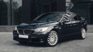 一輛黑色 BMW 轎車停在一棟現代玻璃建築前的鋪面上。.