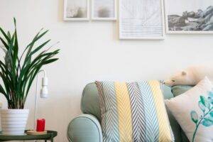 粉綠色的沙發配上圖案鮮明的坐墊，側桌上放著盆栽，白色牆面上掛著有框的藝術品。.