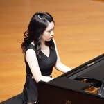 一位身穿黑色禮服的女士正在木製舞台上彈奏三角鋼琴。.