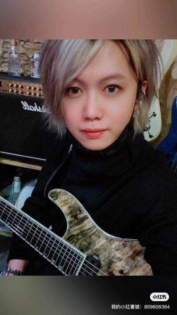 淺色頭髮的人抱著電吉他，坐在 Marshall 擴大機前，看著攝影機。.