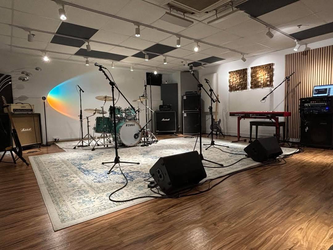 音樂排練室，鼓組、鍵盤、擴大器、麥克風和喇叭排列在木地板上的地毯上。.